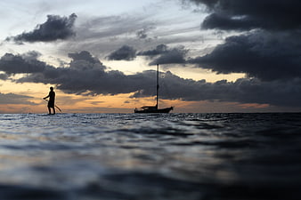 Silhouette of paddleboarder and sailboat at sunset