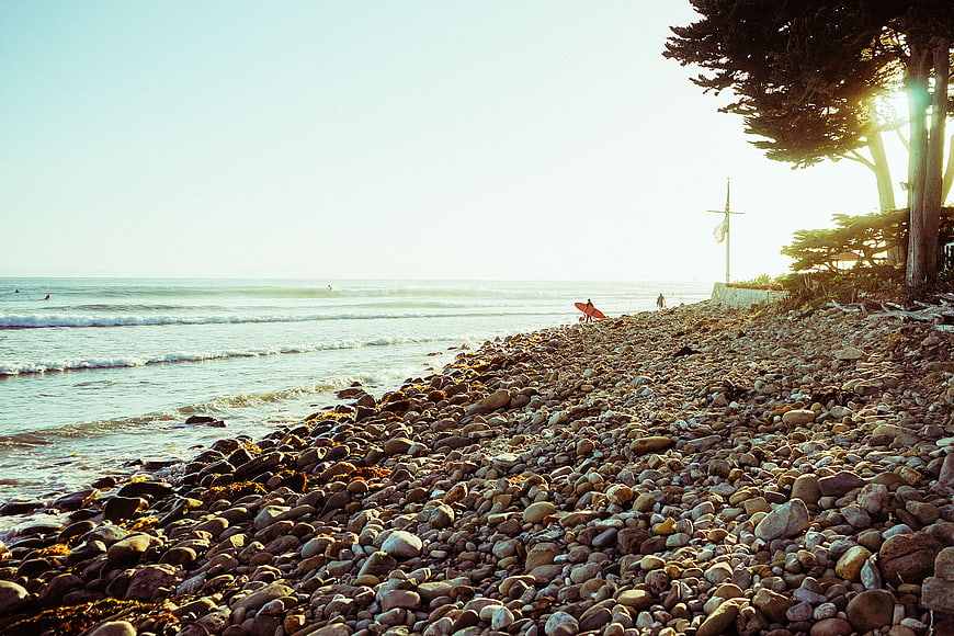 Surfer with red board on rocky beach at sunset