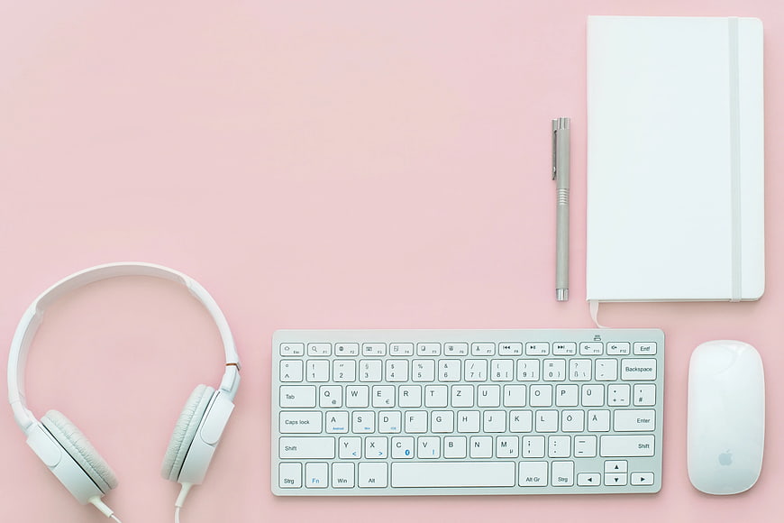 Minimalist pink workspace with white keyboard, mouse, and headphones