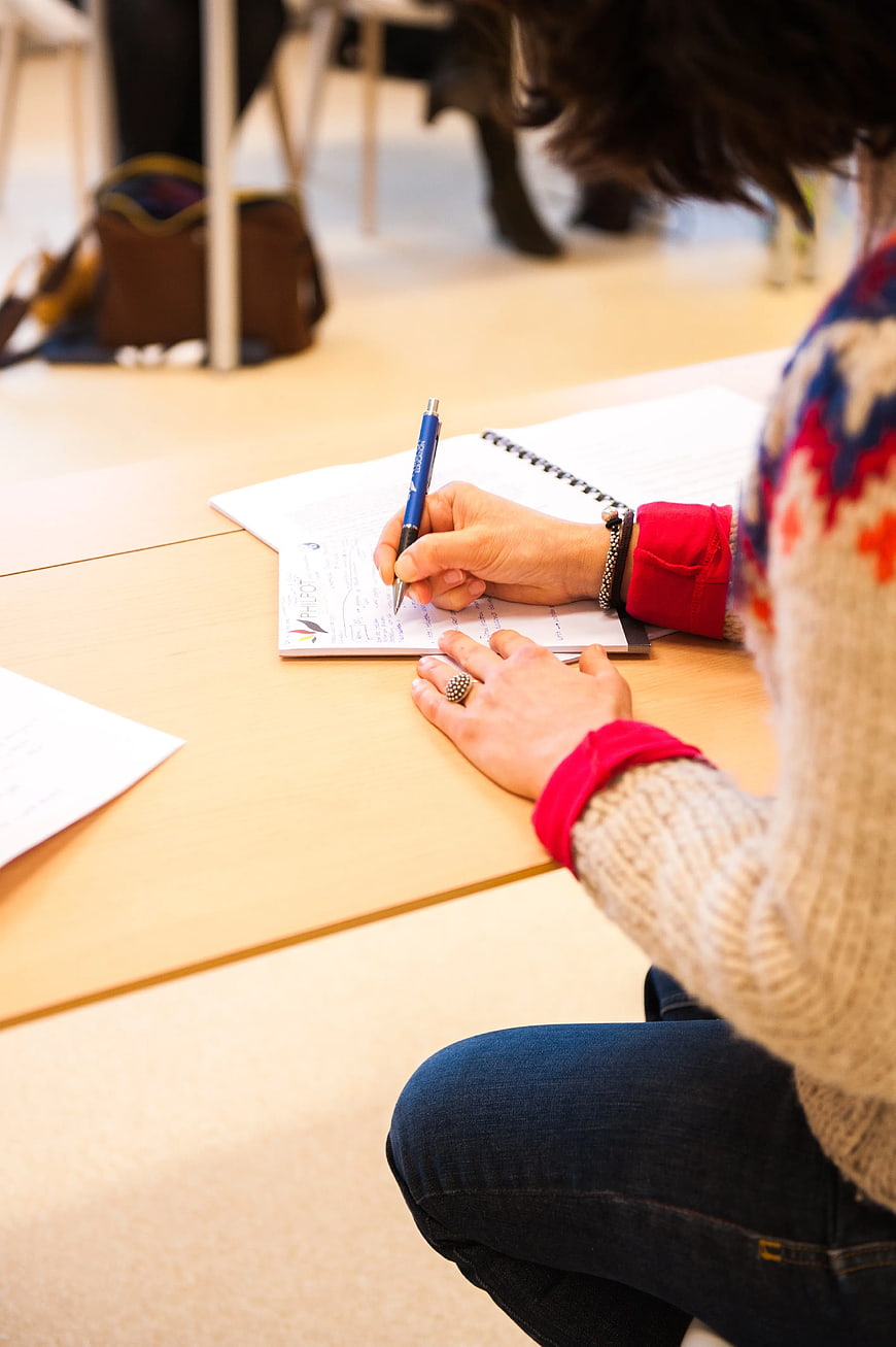 Woman Writing on Paper with Blue Pen at Desk
