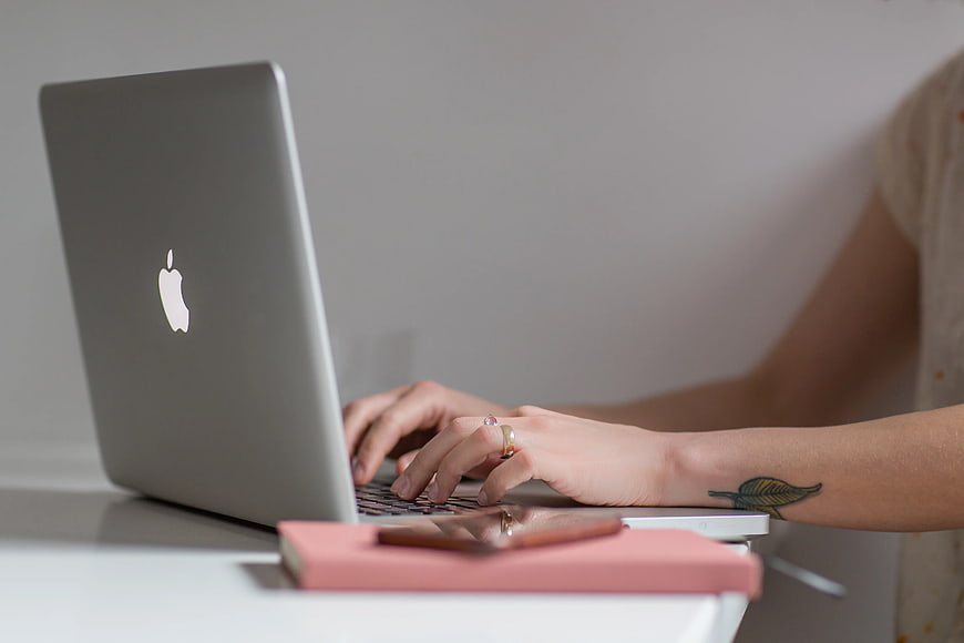 Woman Typing on Laptop with Pink Notebook