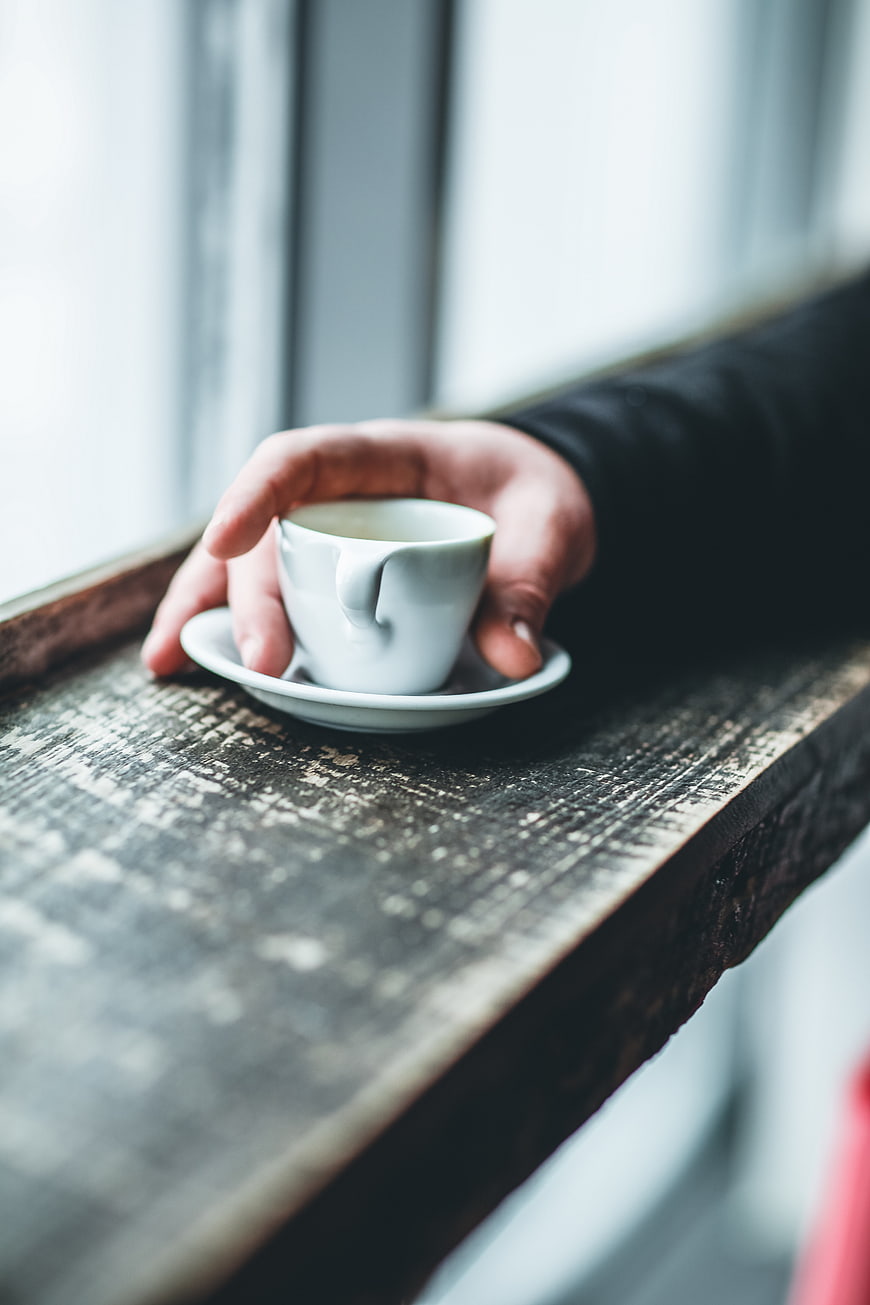 Hand holding white coffee cup on rustic wooden window ledge