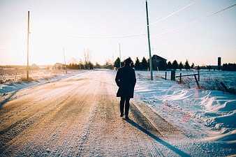 Man Walking Alone on Snowy Rural Road at Sunset