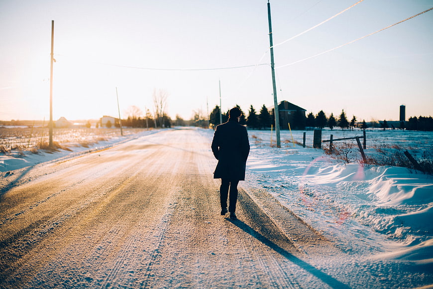 Man Walking Alone on Snowy Rural Road at Sunset