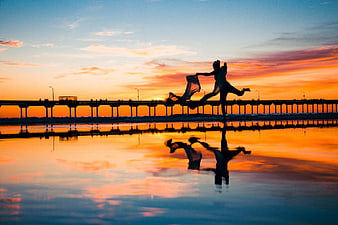 Silhouette of Woman Dancing on Beach at Sunset with Pier Reflection