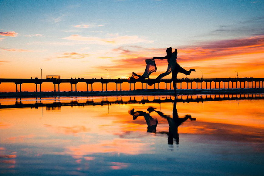 Silhouette of Woman Dancing on Beach at Sunset with Pier Reflection