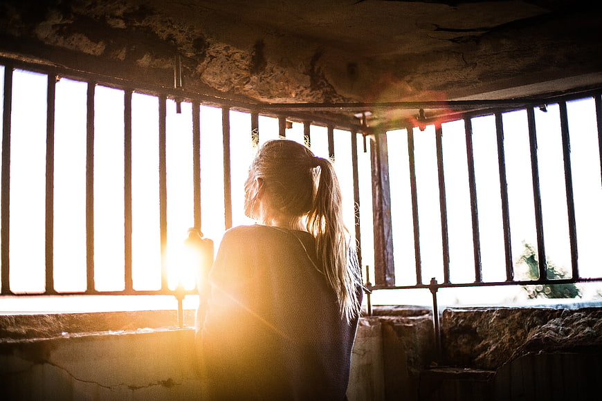 Woman Looking Through Prison Bars at Sunset