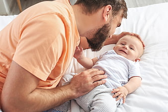 Happy Father Playing with Smiling Baby on White Bed