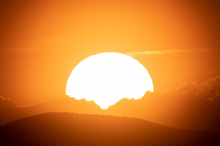 Giant Orange Sun Setting Behind Silhouetted Mountain Ridge