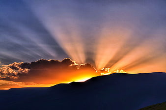 Dramatic Sunset with Sun Rays Over Silhouetted Mountain Ridge