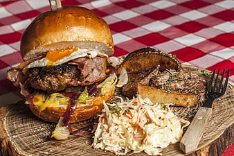 Gourmet burger with egg, bacon, fries, and coleslaw on rustic wood