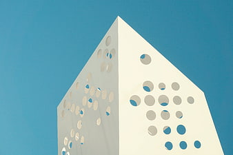 Modern white geometric building with circular cutouts against blue sky