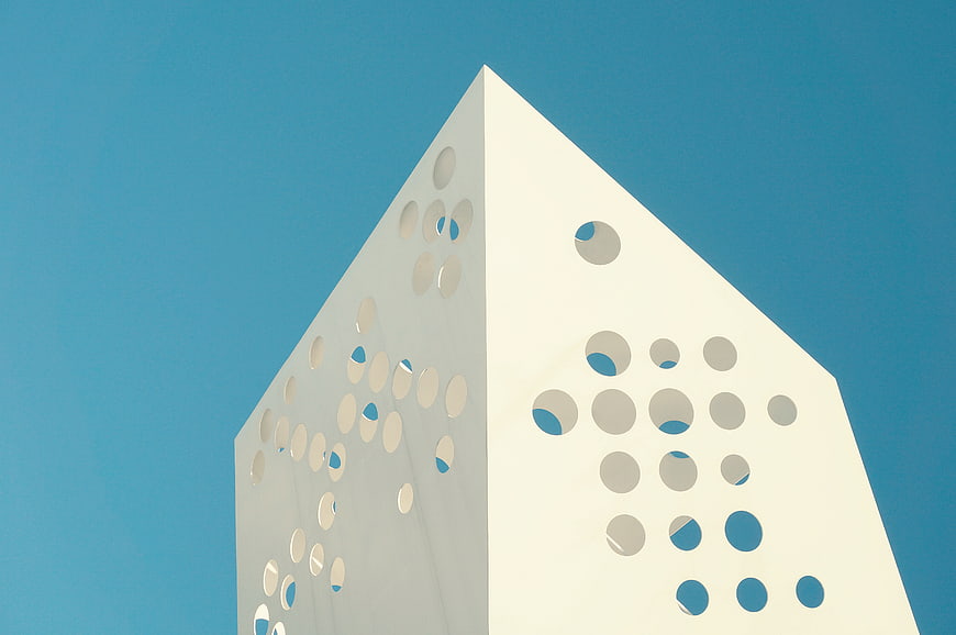 Modern white geometric building with circular cutouts against blue sky
