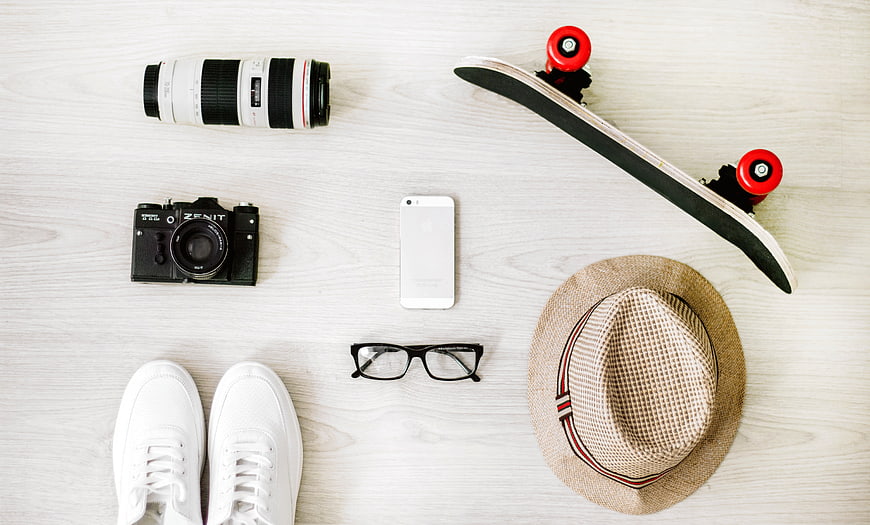 Flat lay of camera, lens, skateboard, hat, and sneakers on white wood