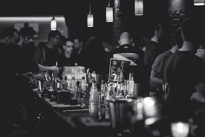 Crowded Bar Scene With Bottles And Hanging Lamps In Black And White