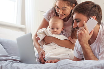 Happy family with baby using laptop and smartphone on bed