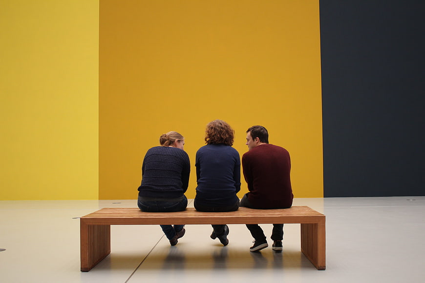 Three people sitting on bench in modern art gallery