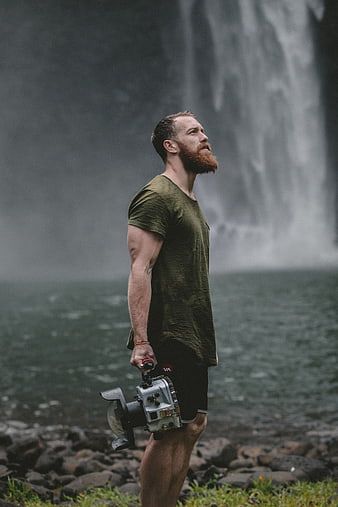 Man with underwater camera standing before waterfall