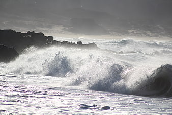 Powerful ocean wave crashing against dark rocky coastline