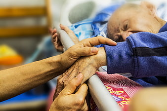 Close-up of caregiver holding elderly patient's hand in hospital bed