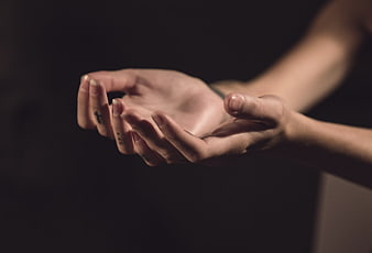 Close-up of cupped hands with cross tattoo on dark background