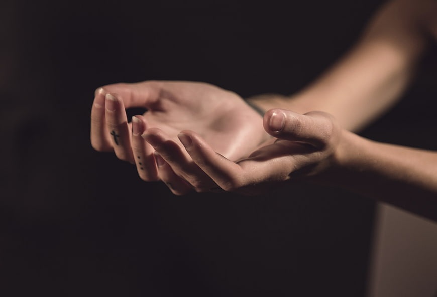 Close-up of cupped hands with cross tattoo on dark background