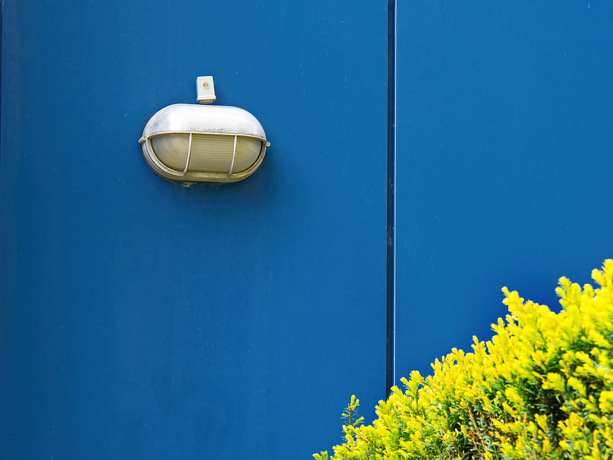 Silver outdoor lamp on blue wall with yellow flowers