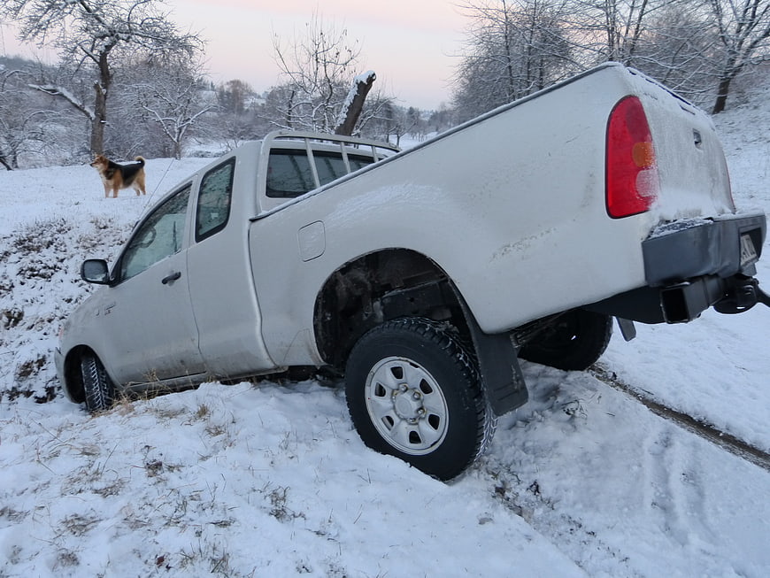 Damaged white pickup truck stuck in deep snow with dog in background