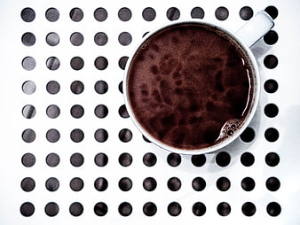 Top view of black coffee in white cup on perforated surface