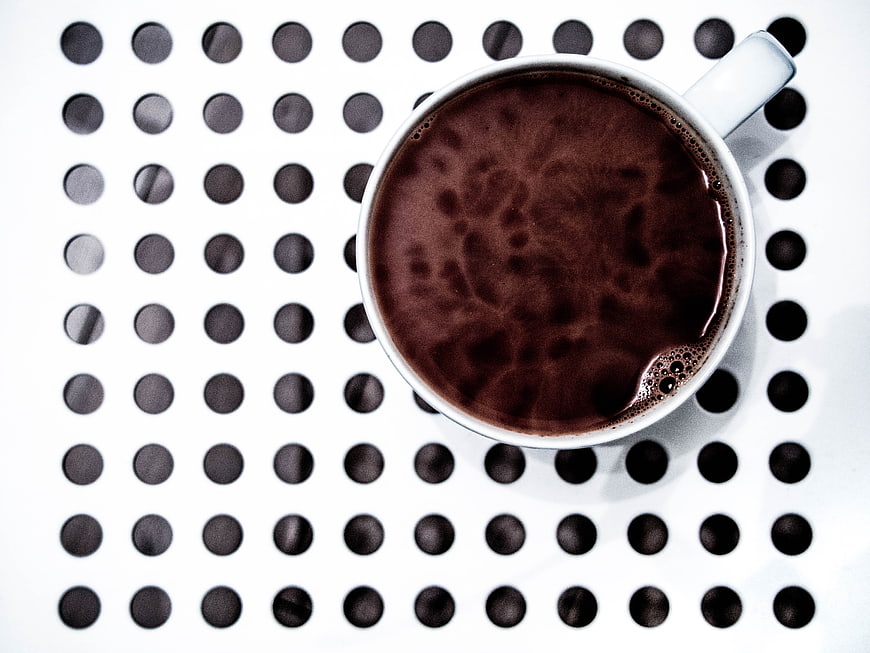 Top view of black coffee in white cup on perforated surface