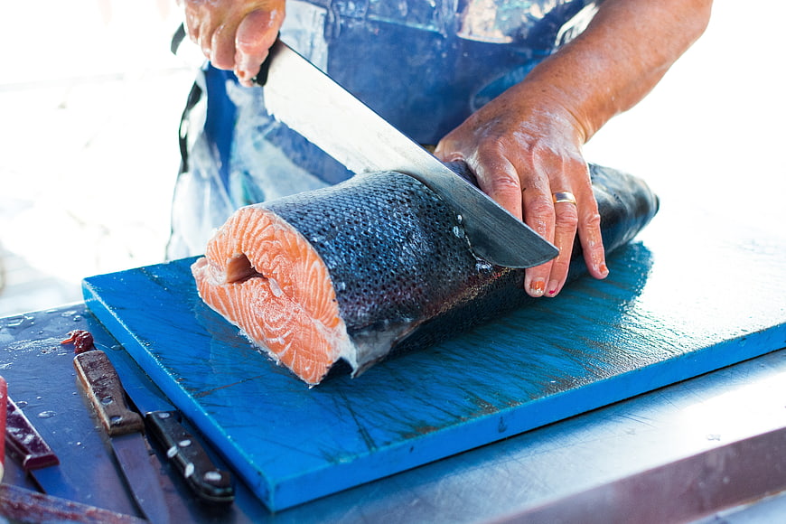 Fishmonger cutting fresh salmon on blue cutting board