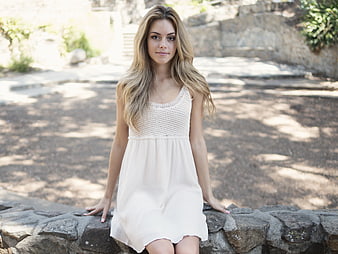 Young woman in white dress sitting on stone wall outdoors