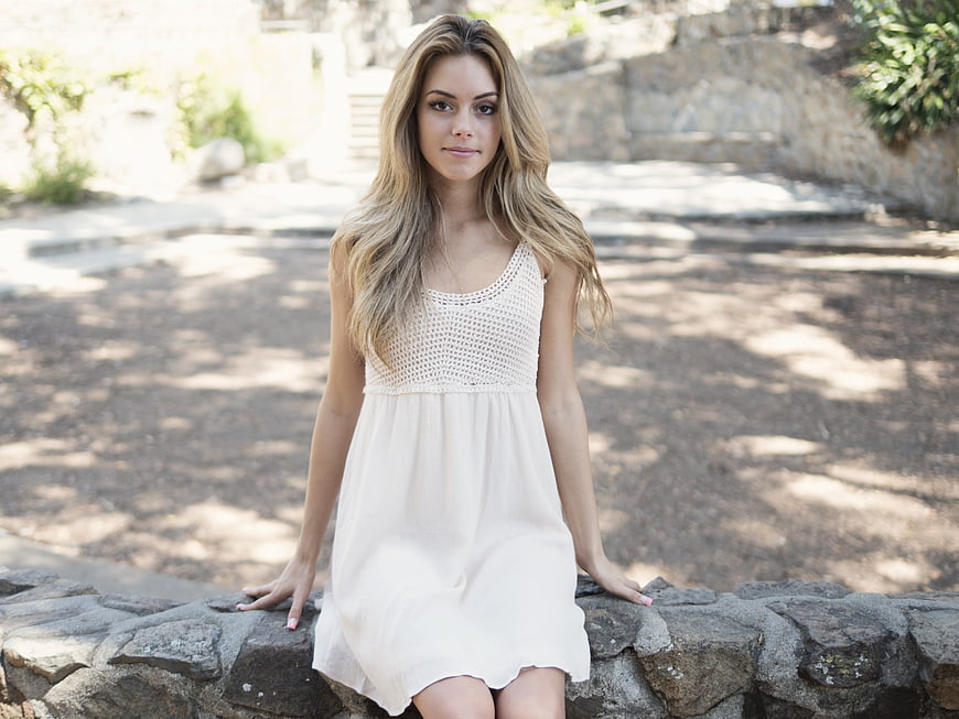 Young woman in white dress sitting on stone wall outdoors