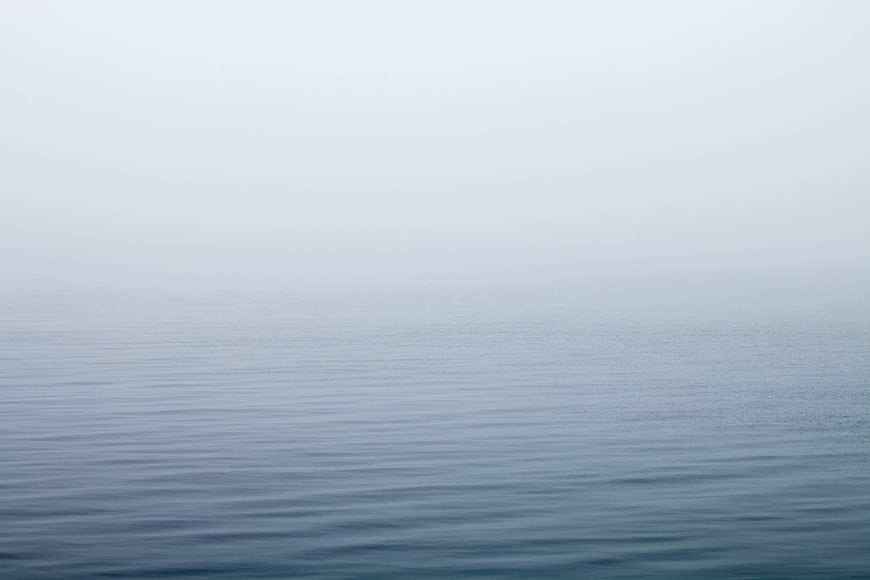 Minimalist foggy ocean horizon with calm water ripples