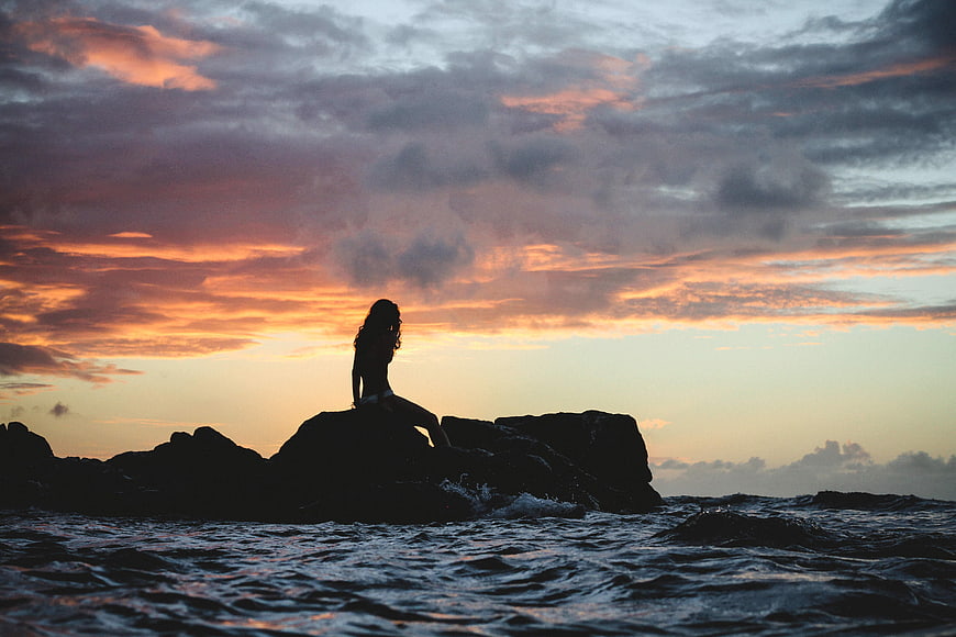 Silhouette of Woman Sitting on Rocks at Sunset