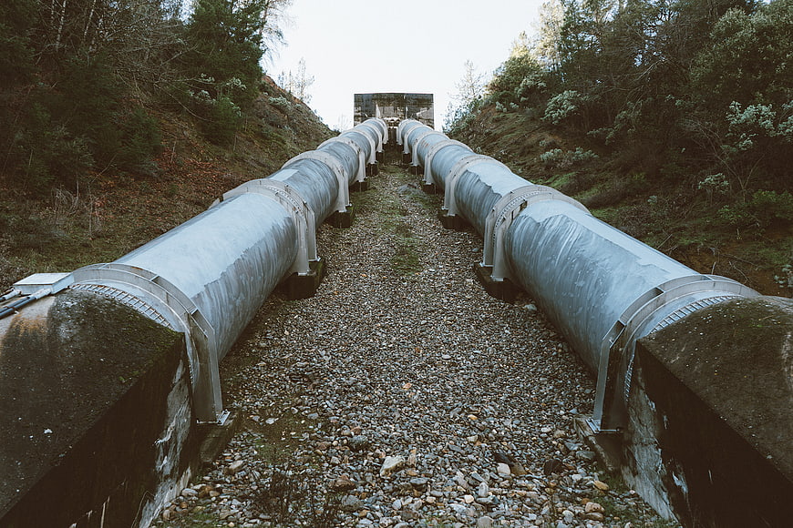Parallel steel pipelines running through a forested gravel path
