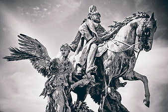 Black and white low-angle shot of a weathered equestrian statue with an angel