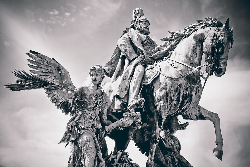 Black and white low-angle shot of a weathered equestrian statue with an angel