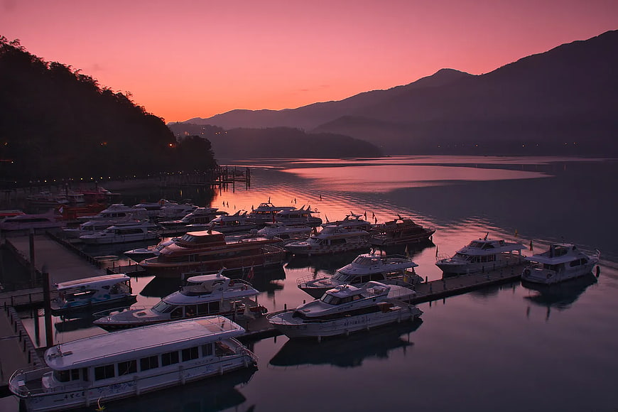 Boats docked at marina during pink sunset with mountains