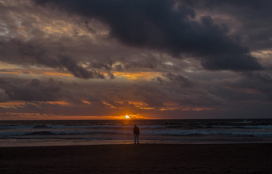 Silhouette of Man Standing on Beach at Dramatic Sunset