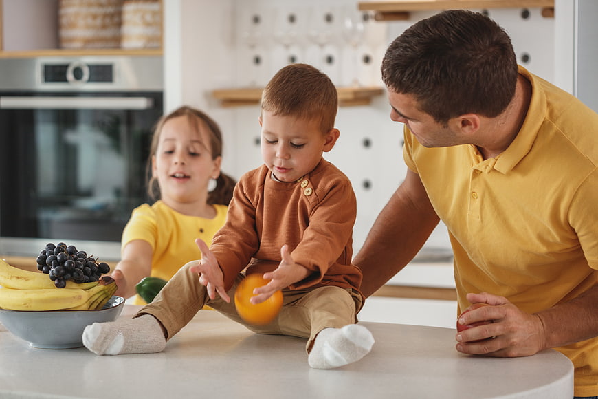 Father and children playing with fruit in modern kitchen