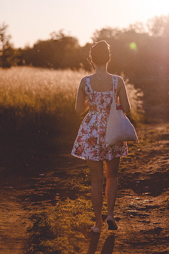 Woman in Floral Dress Walking on Dirt Path at Sunset