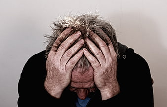 Senior man holding head in hands expressing deep distress and despair