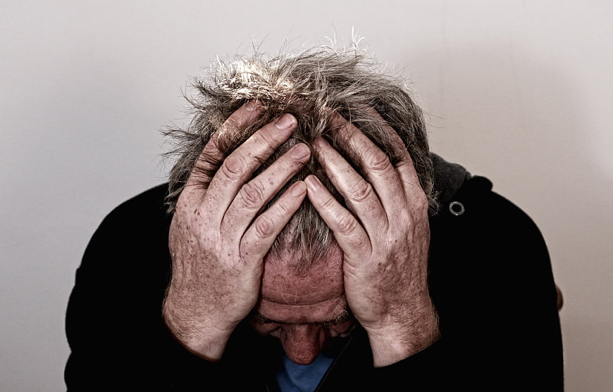 Senior man holding head in hands expressing deep distress and despair