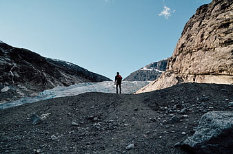 Hiker with red backpack standing on rocky glacier moraine