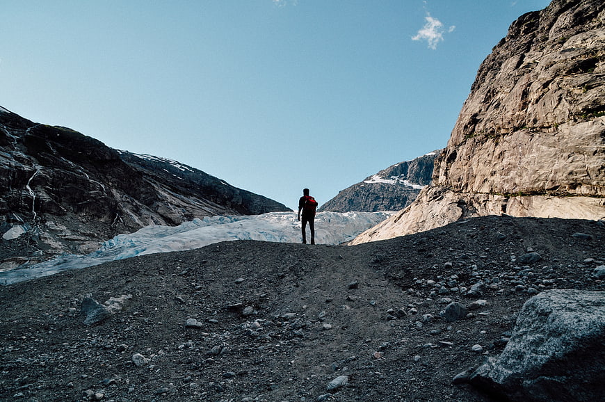 Hiker with red backpack standing on rocky glacier moraine