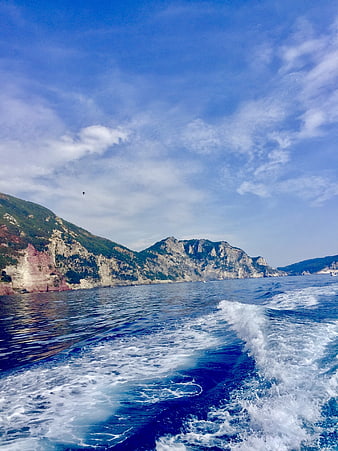 Boat wake on blue sea with rocky cliffs and mountains