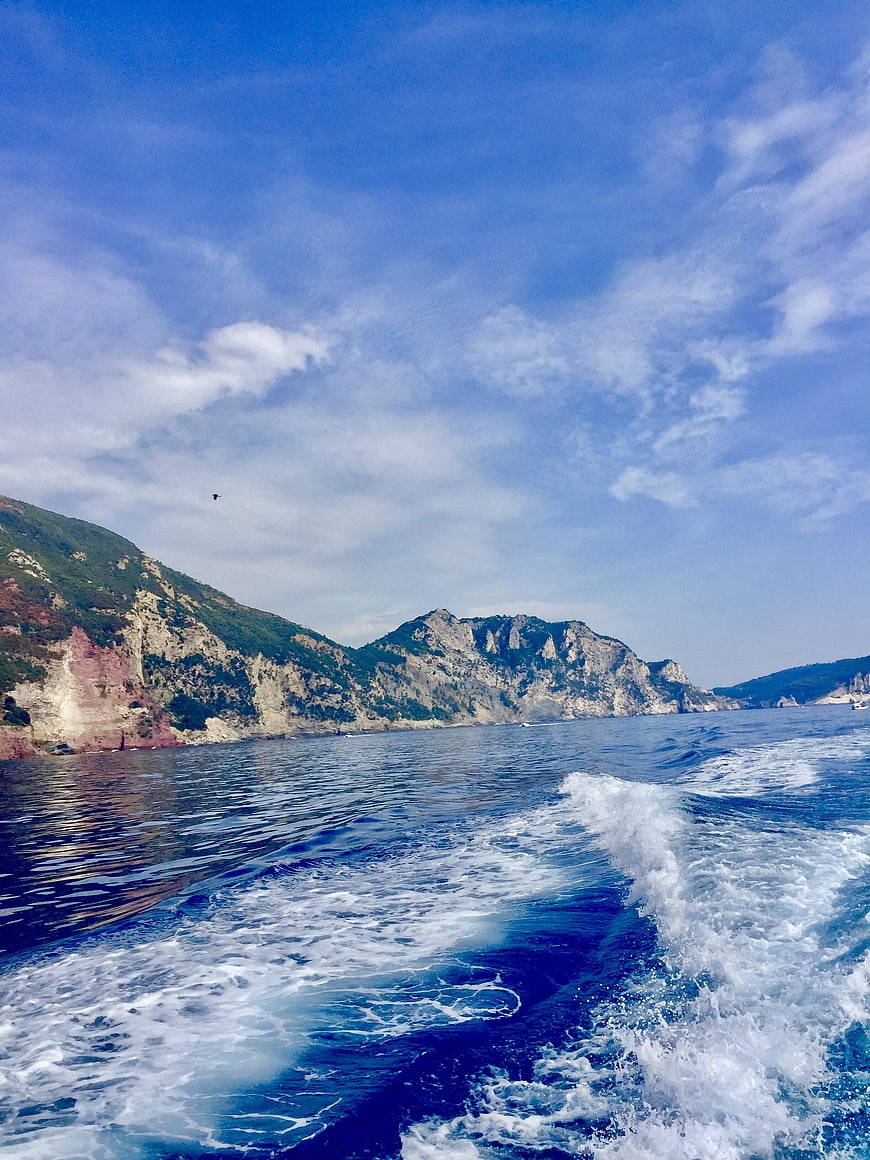 Boat wake on blue sea with rocky cliffs and mountains