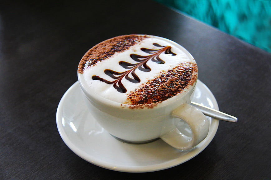 Cappuccino with chocolate leaf art on dark table