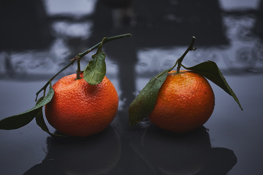 Two Fresh Oranges with Leaves on Dark Wet Surface